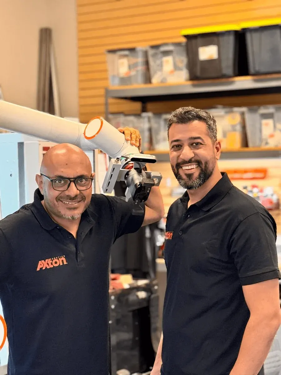 Michael Nessim and Malak Mitch of Axton Robotics holding a cobot arm with a robotic gripper used for CNC machine tending