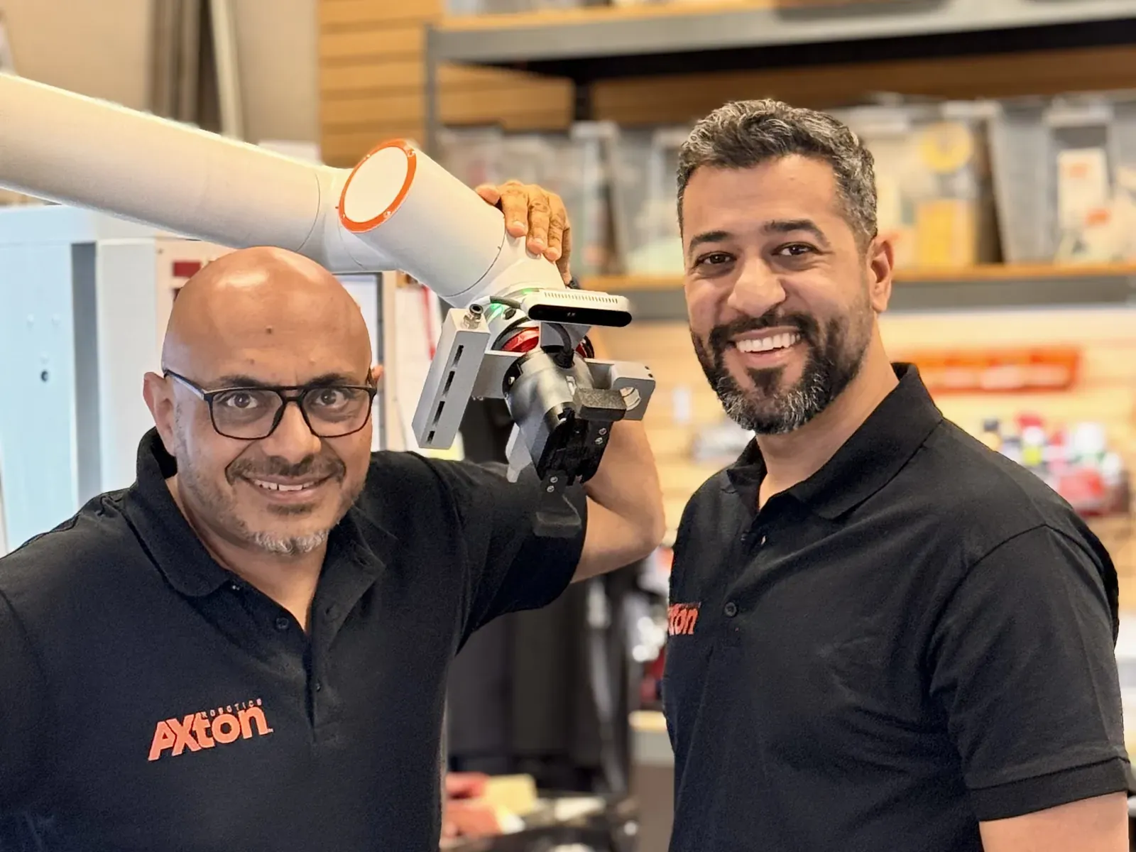 Michael Nessim and Malak Mitch of Axton Robotics holding a cobot arm with a robotic gripper used for CNC machine tending
