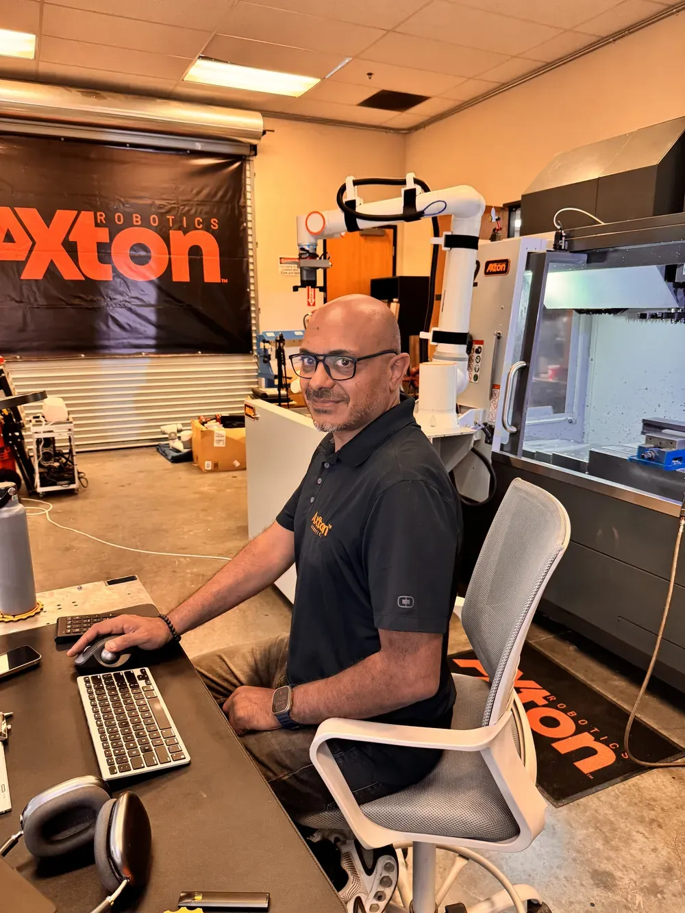 Michael Nessim programming at a desk with a cobot arm behind him in the Axton Robotics lab