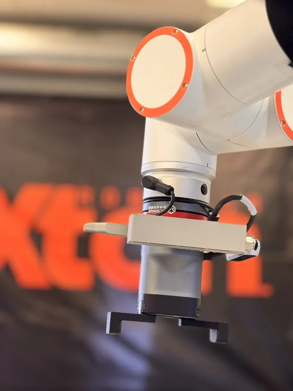 Close-up of a cobot arm and robotic gripper in front of the Axton Robotics banner