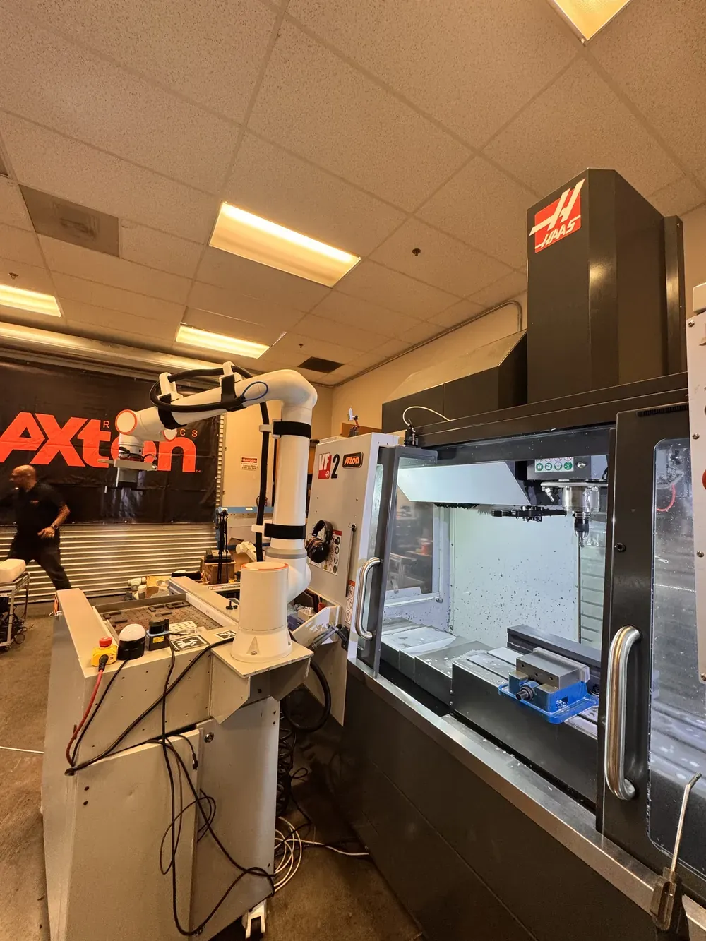 Axton Robotics cobot machine tending cell beside a Haas CNC mill, with the Axton banner behind it