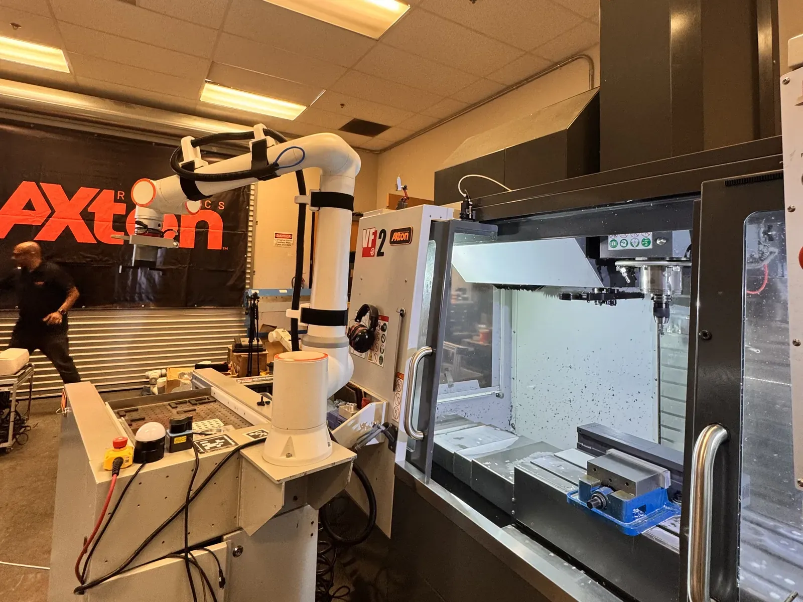 Axton Robotics cobot machine tending cell beside a Haas CNC mill, with the Axton banner behind it