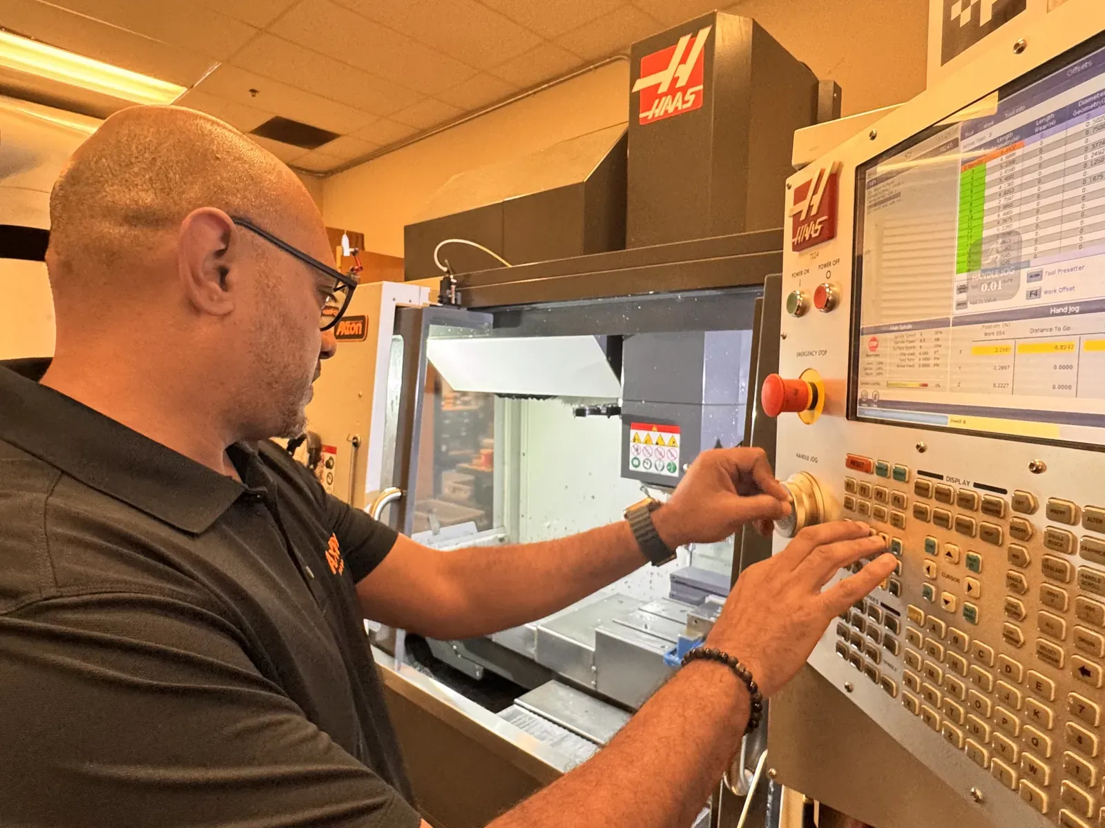 Michael Nessim at a Haas CNC control panel with an AprilTag marker above the screen for robot alignment