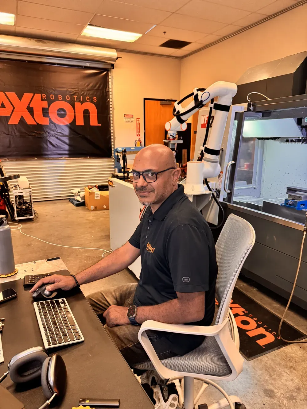 Michael Nessim programming a cobot at his desk with the robot arm behind him in the Axton Robotics lab