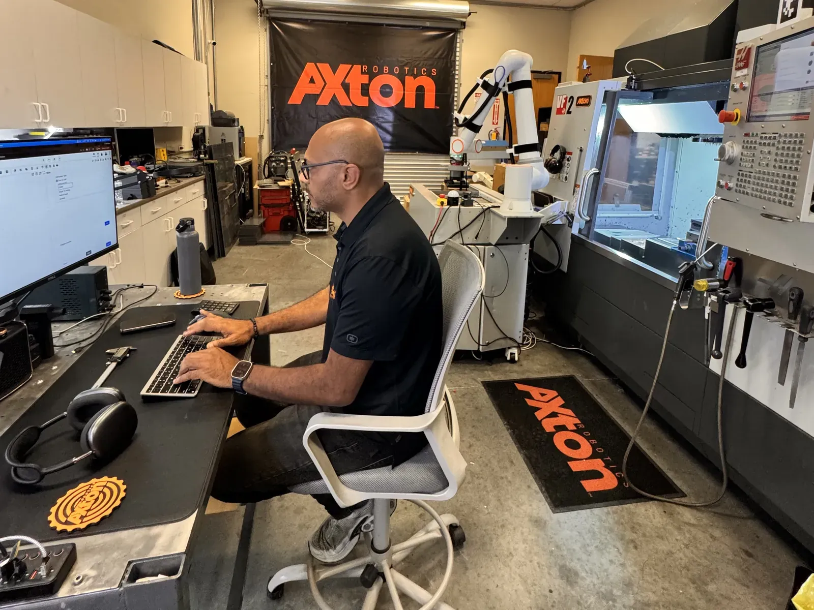 Michael Nessim programming a cobot at his desk with the robot arm behind him in the Axton Robotics lab