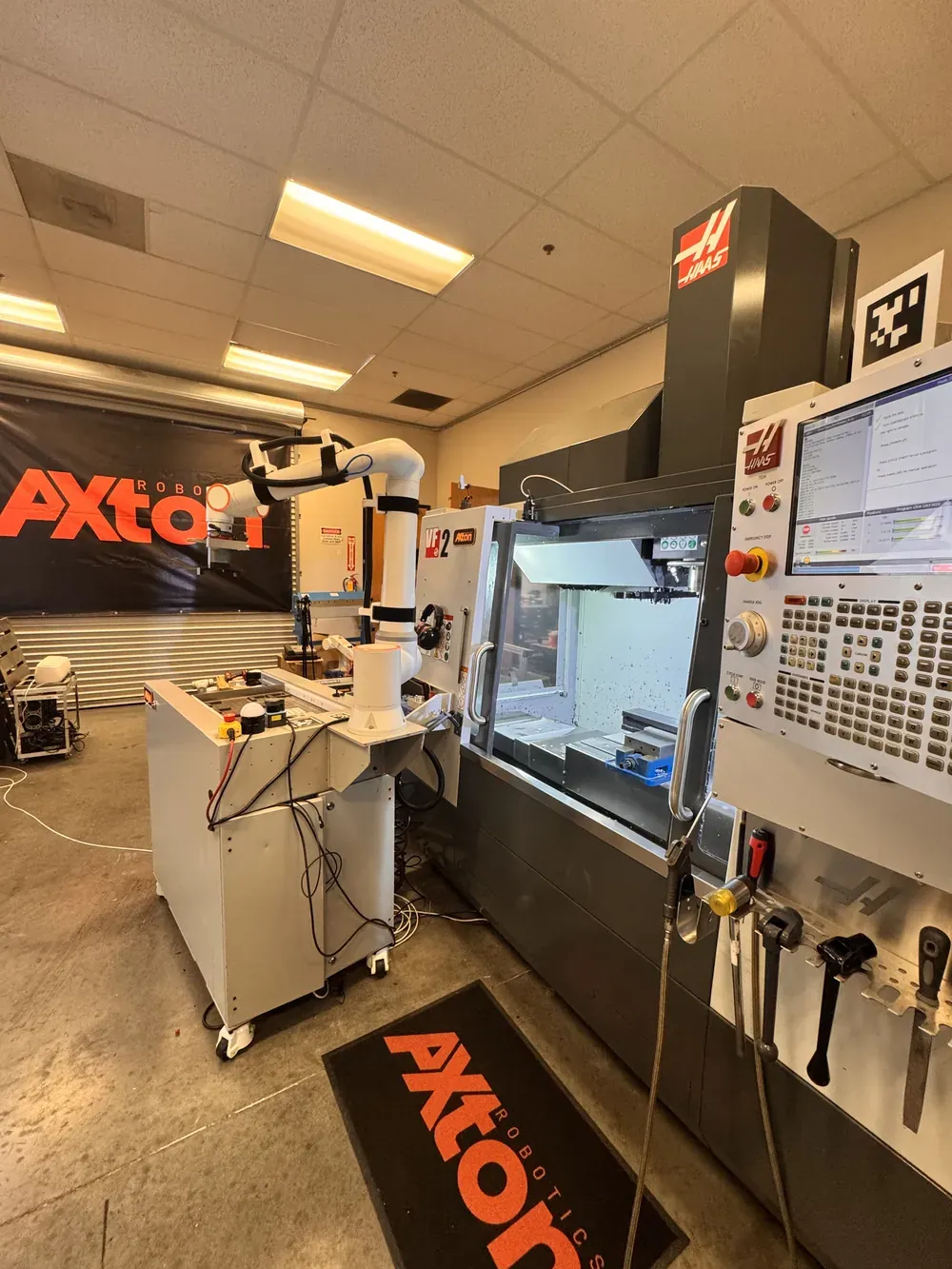 Mobile Axton Robotics machine tending station on wheels beside a Haas CNC mill