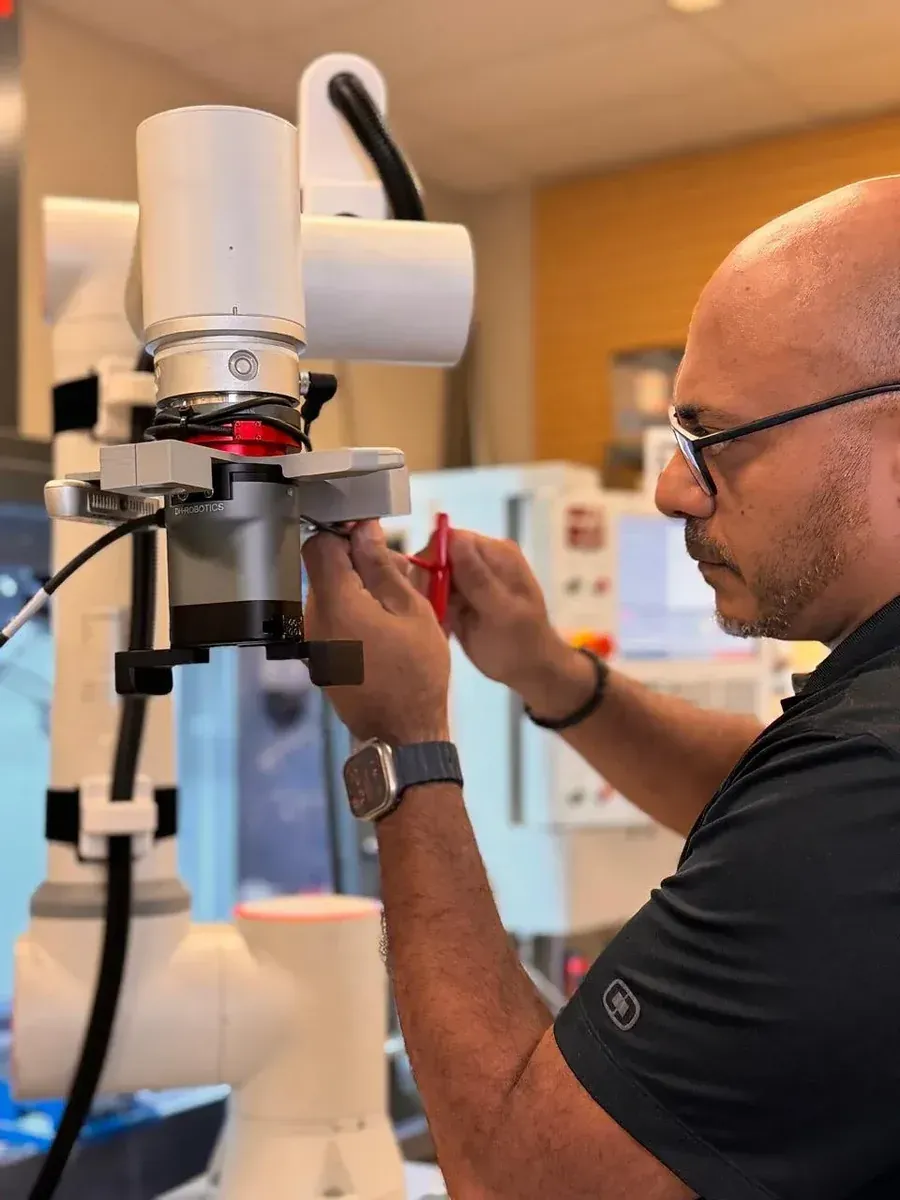 Axton Robotics engineer adjusting a robotic gripper on a cobot arm while prototyping a CNC machine tending cell